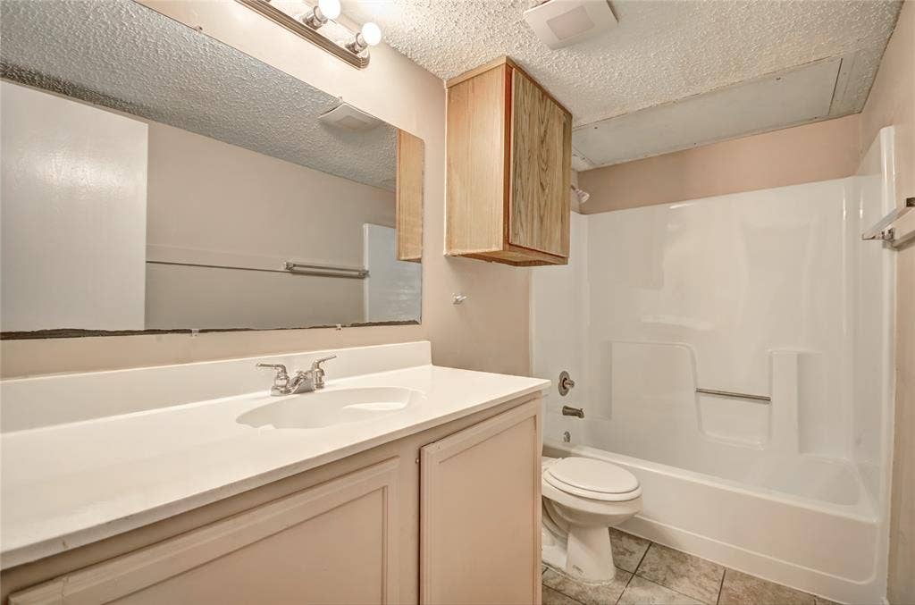 1912 Bernice Street, #B, Haltom City, TX 76117 Bathroom featuring a vanity with an integrated sink, a large wall-mounted mirror, a separate wood-finish wall cabinet, seating area, and a combined shower-tub unit