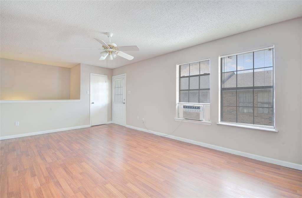 1912 Bernice Street, #B, Haltom City, TX 76117 Spacious interior featuring luxury plank flooring, two large windows with blinds, a ceiling fan, and a half-wall architectural detail