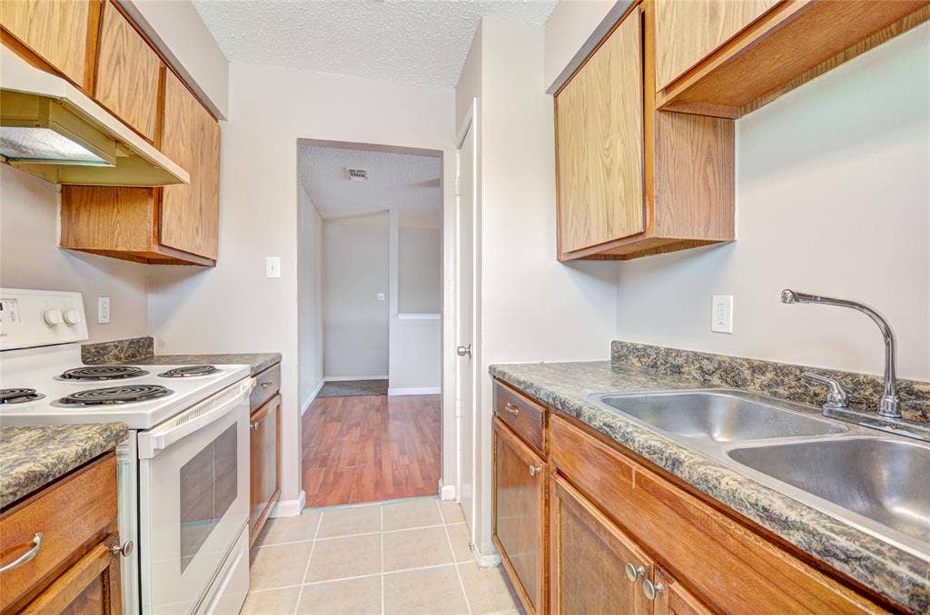 1912 Bernice Street, #B, Haltom City, TX 76117 Galley kitchen featuring wood-finish cabinetry, upgraded countertops, and white appliances