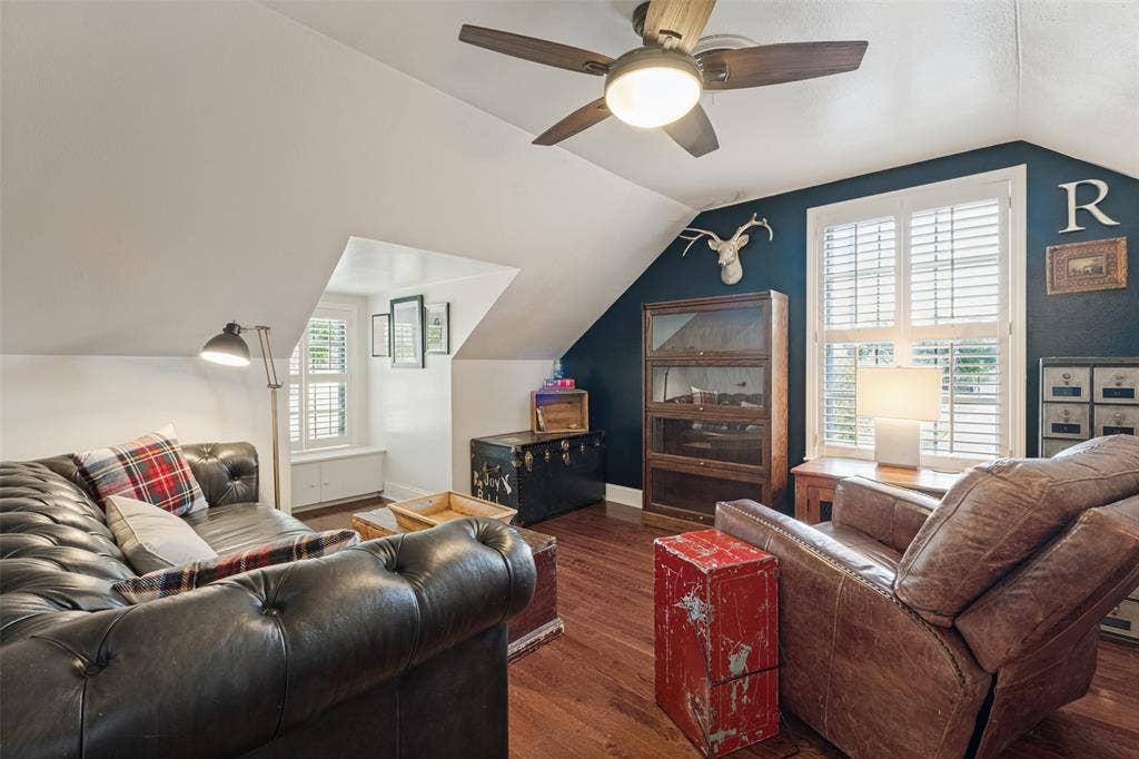 Vaulted ceilings featuring a central ceiling fan with integrated lighting, wood-finish flooring, and white plantation-style shutters