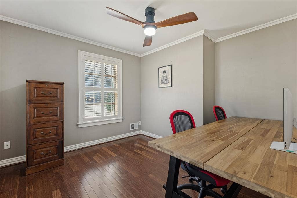 Room with dark wood-finish flooring, neutral wall tones, crown molding, a window with interior shutters, and a three-blade ceiling fan