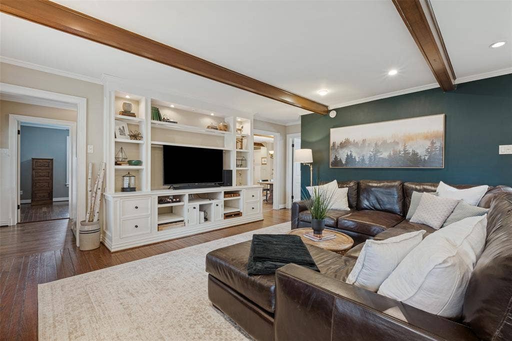 Living area featuring exposed wooden ceiling beams, built-in white cabinetry with open shelving, and dark-toned accent wall