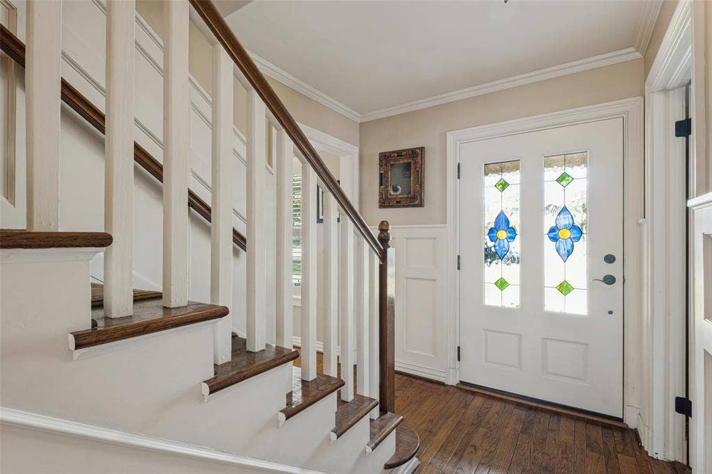 Entryway featuring a white door with stained glass inserts, wood-finish flooring, wainscoting, and a staircase with a wooden handrail and balusters