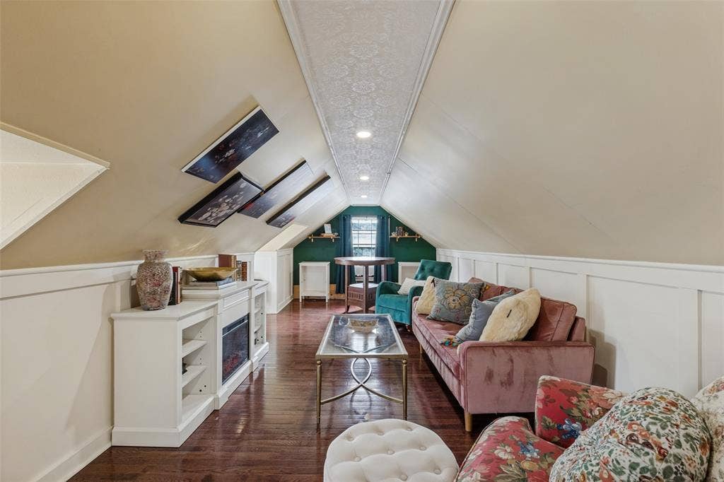 Finished attic featuring wood-finish flooring, white board-and-batten wainscoting, recessed ceiling lighting, and a built-in media console with an integrated electric fireplace