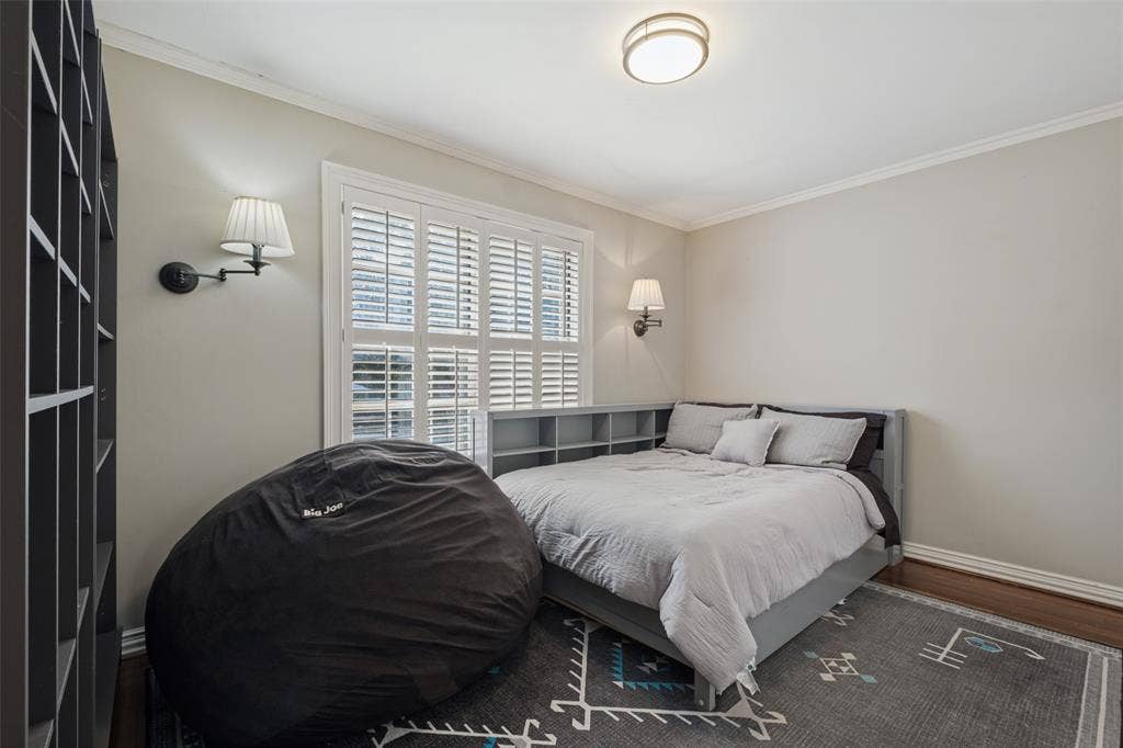 Room featuring wood-finish flooring, plantation shutters, dual wall-mounted sconces, and a ceiling-mounted light fixture