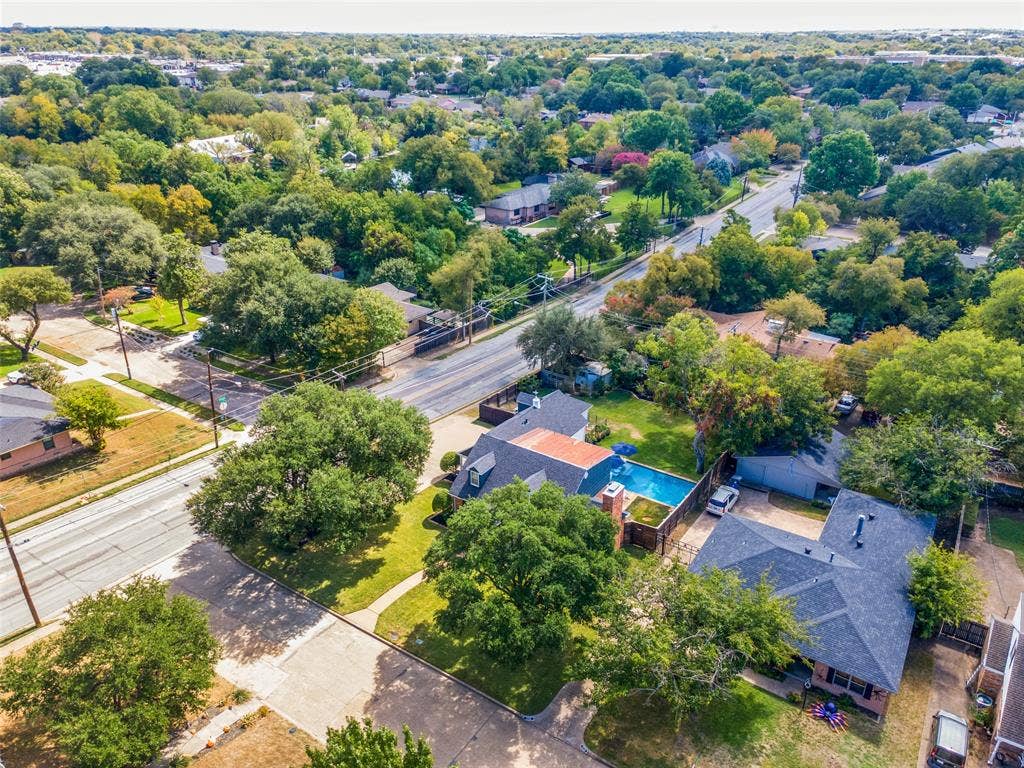 Aerial view featuring a residential property with a swimming pool, asphalt shingle roofing, brick masonry exterior, and mature trees on the lot