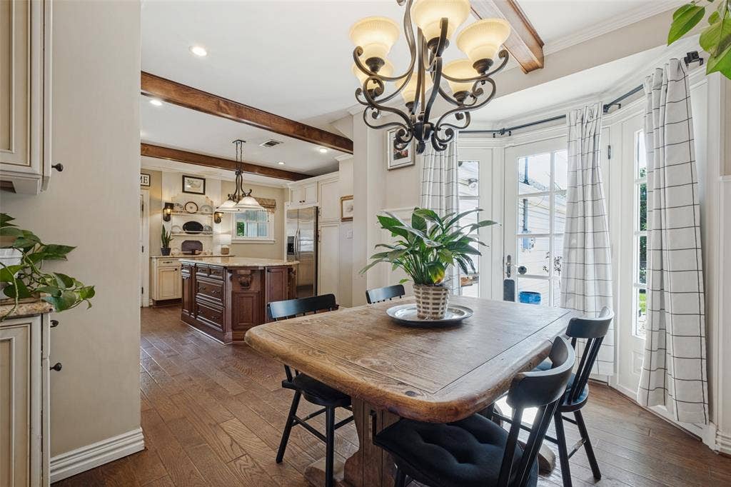 Kitchen featuring wood-finish flooring, exposed ceiling beams, a central island with stone-finish countertops, and a multi-arm iron chandelier