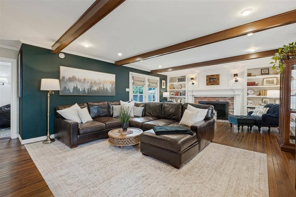 Living area featuring dark-stained wood-finish flooring, exposed ceiling beams, a brick-surround fireplace, and built-in shelving