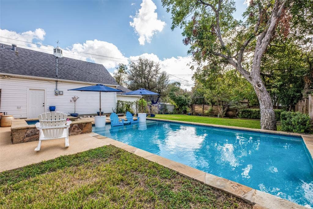 In-ground swimming pool featuring stone coping, integrated raised stone spa, concrete hardscaping, and mature trees