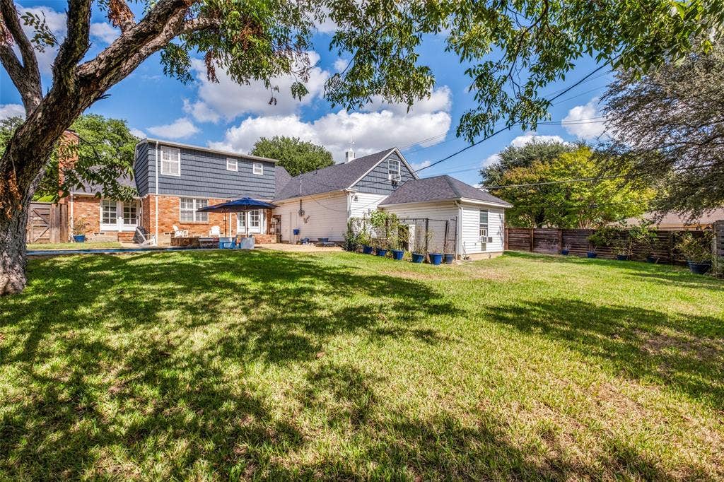 Expansive backyard featuring a large grass lawn, mature shade trees, and a wood privacy fence