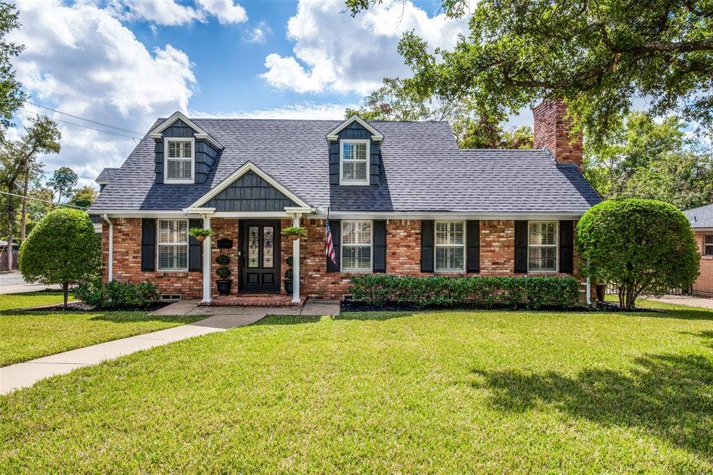 Traditional brick exterior featuring a steeply pitched roof, cedar-shake accents, gabled dormers, and a covered front porch with decorative columns