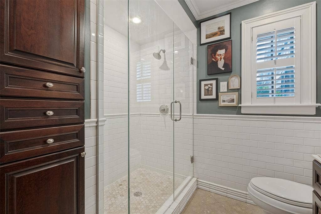 Walk-in shower featuring a glass enclosure, white subway tile surround, and stone pebble flooring, complemented by dark wood cabinetry and interior window shutters