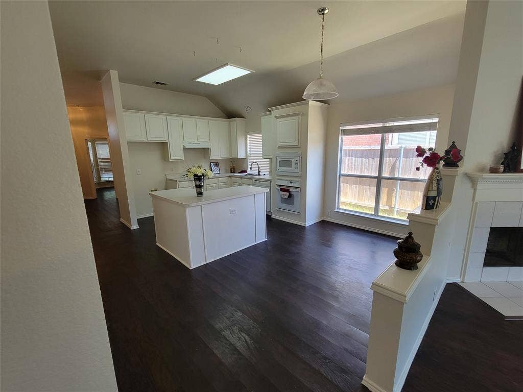 Kitchen featuring white cabinets, dark wood-type flooring, and a center island open to breakfast room and open hallway