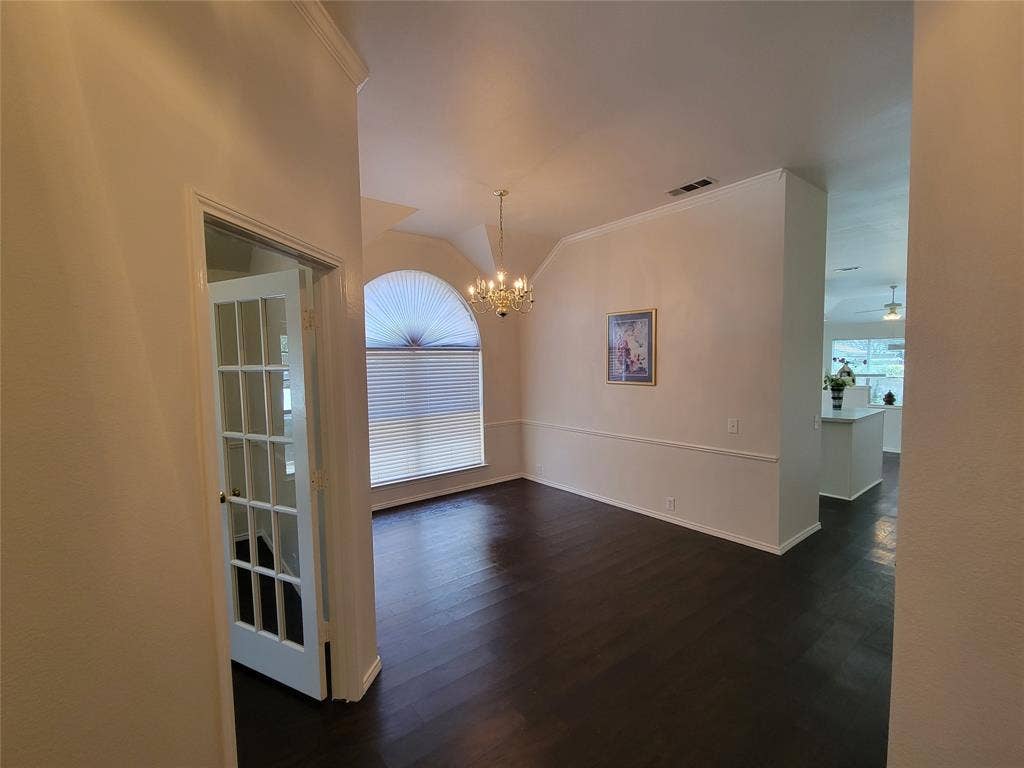 Entryway looking at dining room with chandelier, dark wood-style flooring, vaulted ceiling, and ornamental molding