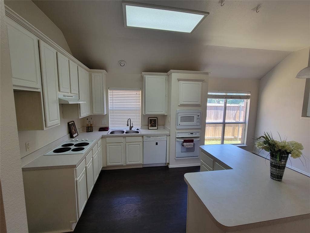 Kitchen with sink, white cabinetry, vaulted ceiling, and white appliances