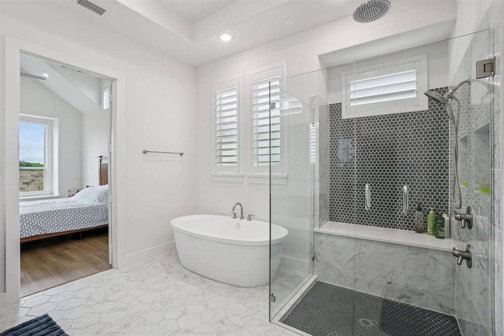 3960 Medio Creek Drive, Prosper, TX 75078 Bathroom featuring a freestanding oval tub, a walk-in shower with clear glass enclosure and dark hexagonal tile, and hexagonal marble-look floor tiles