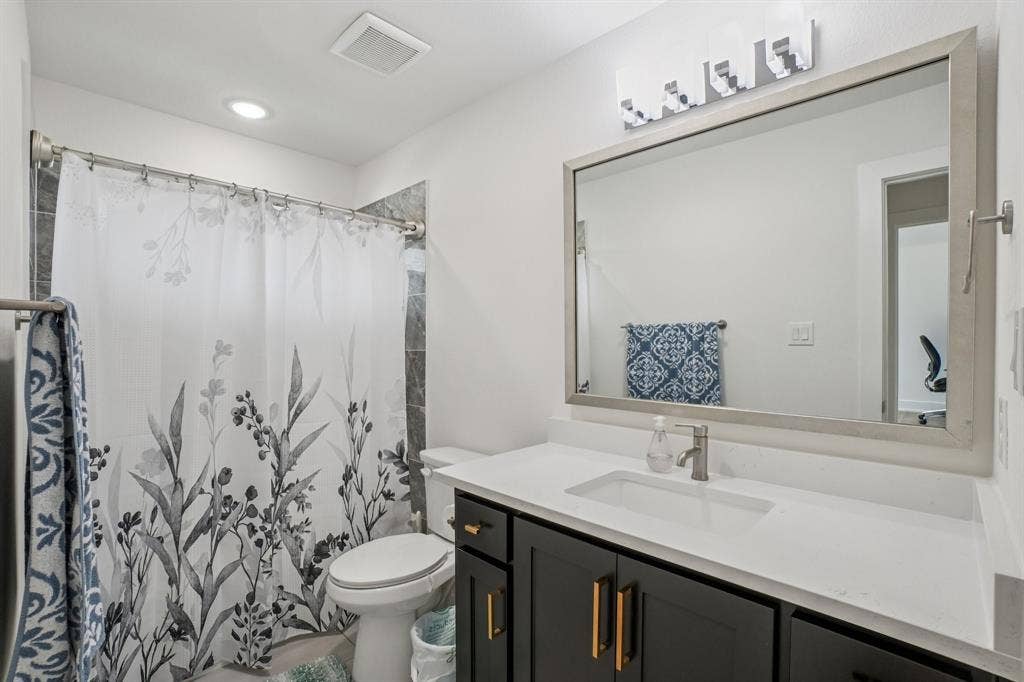 3960 Medio Creek Drive, Prosper, TX 75078 Contemporary bathroom featuring a dark wood-finish vanity with gold-tone hardware, a white undermount sink, and a light-toned countertop