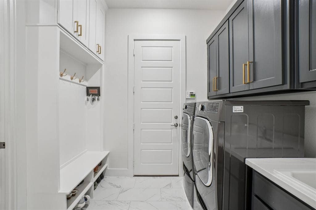 3960 Medio Creek Drive, Prosper, TX 75078 Laundry area featuring a built-in mudroom bench with storage, white shaker-style cabinetry with gold-toned hardware, gray upper cabinetry, marble-look floor tiling, and a utility sink with a countertop