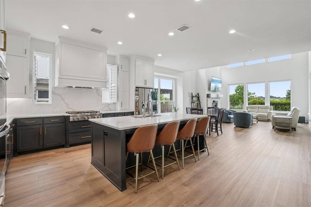 3960 Medio Creek Drive, Prosper, TX 75078 Open-concept kitchen featuring an oversized island with seating, a gas range with a decorative range hood, two-tone cabinetry, and wood-finish flooring