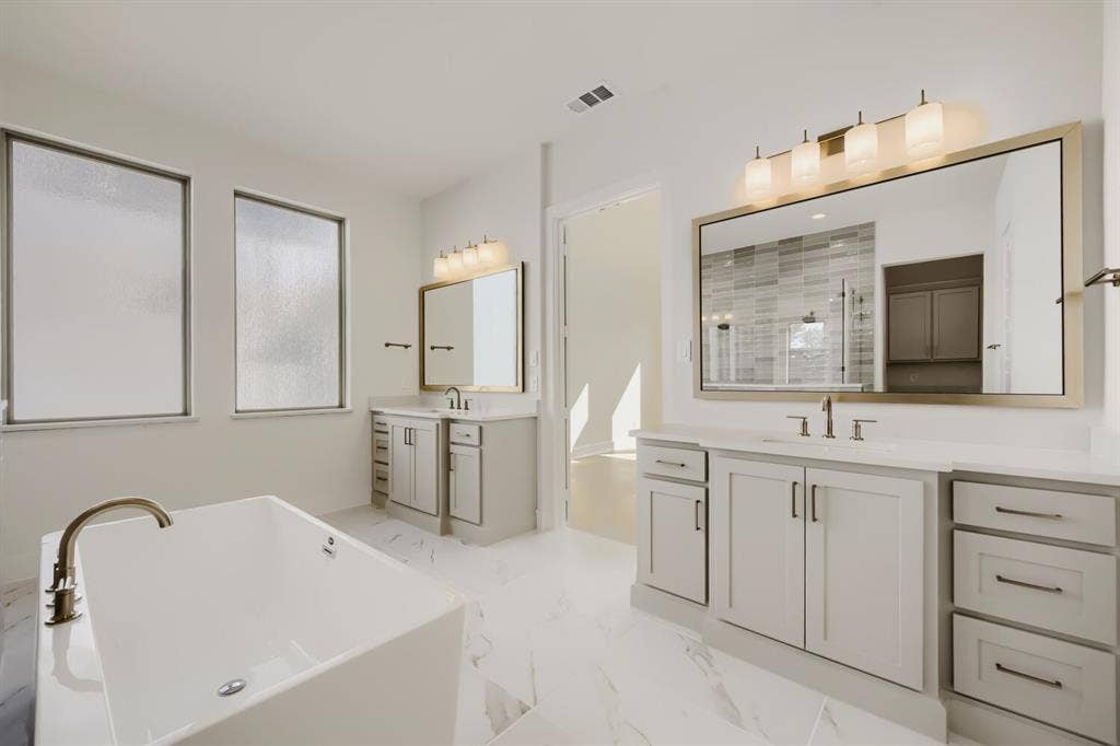 1317 Naples Court, Keller, TX 76248 Freestanding soaking tub with a floor-mounted faucet, dual vanities with integrated sinks, large framed mirrors, and contemporary light fixtures