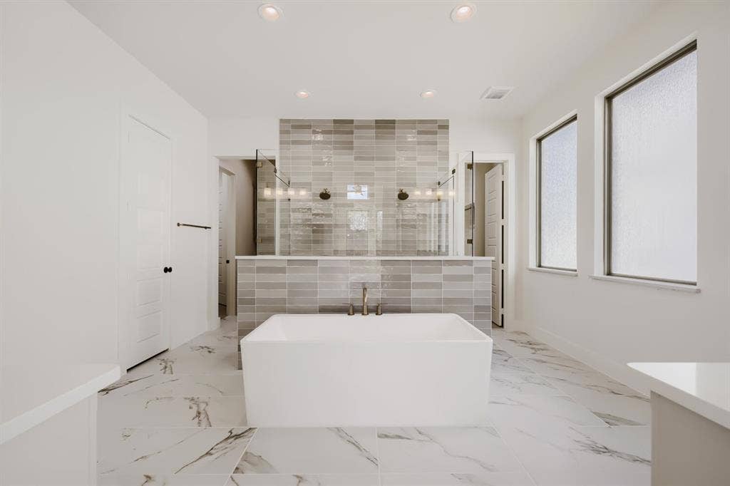 1317 Naples Court, Keller, TX 76248 Freestanding soaking tub with floor-mounted faucet, marble-look tile flooring, and a tiled shower enclosure with glass panels