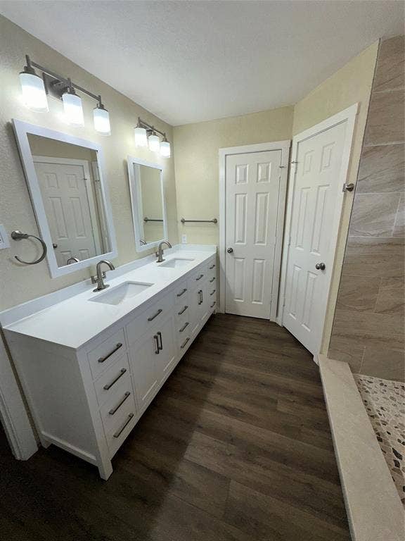 6620 Moss Lane, Watauga, TX 76148 Double vanity with white cabinetry and integrated sinks, quartz countertop, wood-finish flooring, two rectangular framed mirrors, and a tiled shower with a mosaic floor