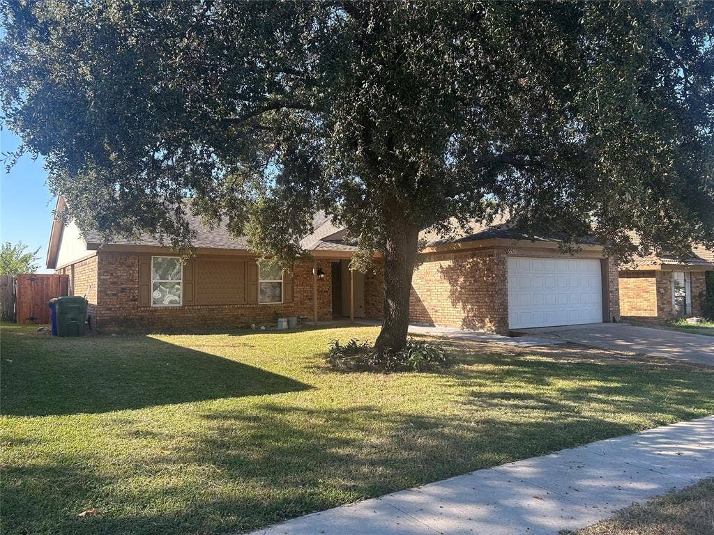 6620 Moss Lane, Watauga, TX 76148 Brick façade home featuring a prominent mature tree, attached two-car garage, and a concrete driveway