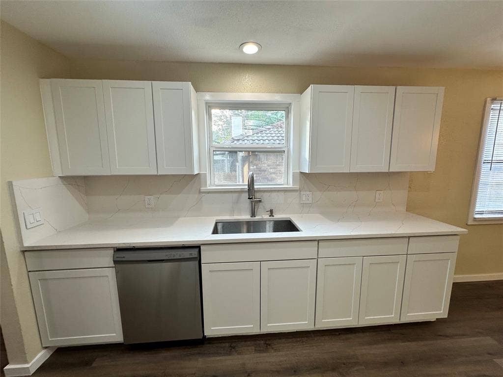 6620 Moss Lane, Watauga, TX 76148 Modern kitchen featuring white shaker cabinetry, stainless steel sink, sleek stainless steel dishwasher, light-toned countertops, and coordinating backsplash
