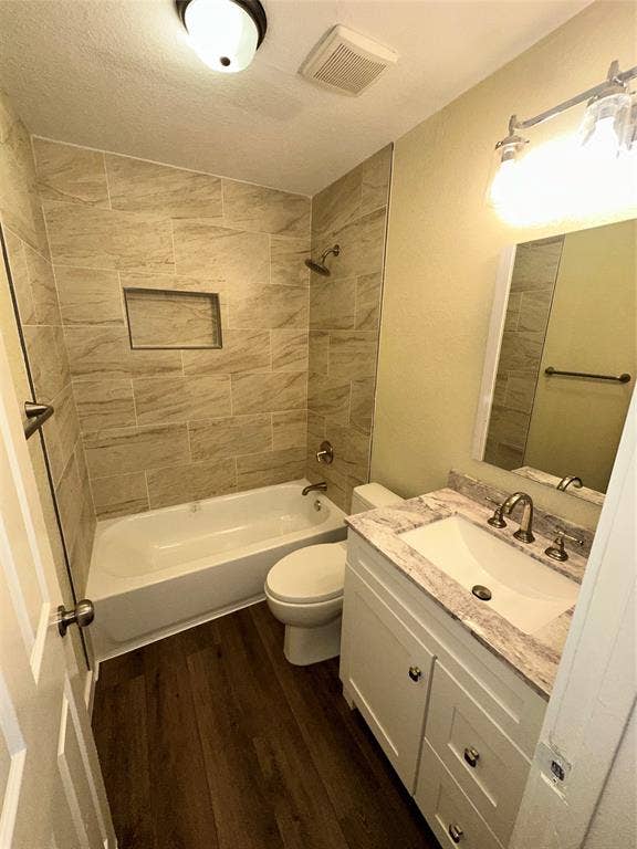 6620 Moss Lane, Watauga, TX 76148 Bathroom featuring a white bathtub, tiled shower surround with an integrated niche, wood-finish flooring, a white vanity with an integrated sink, and a light-colored countertop