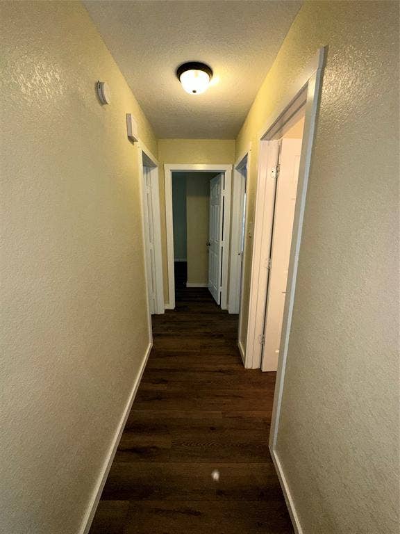 6620 Moss Lane, Watauga, TX 76148 Hallway featuring wood-finish flooring, light-toned walls, multiple doorways, and a flush-mount ceiling light fixture