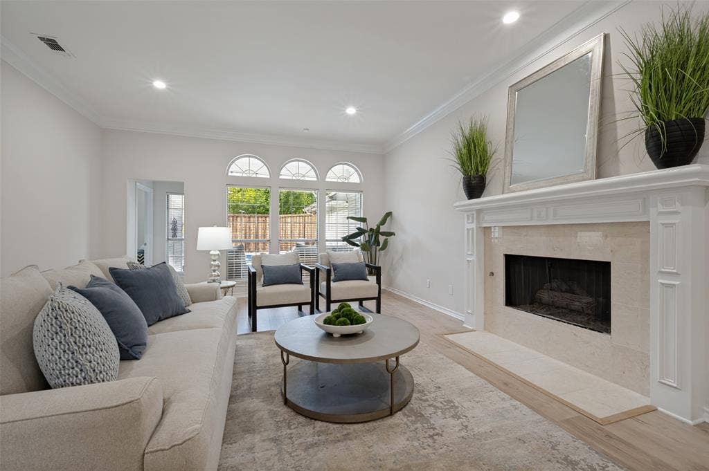 4420 Barwyn Lane, Plano, TX 75093 Living area featuring a classic fireplace with a stone surround and hearth, bright recessed lighting, wood-finish flooring, and multiple arched windows