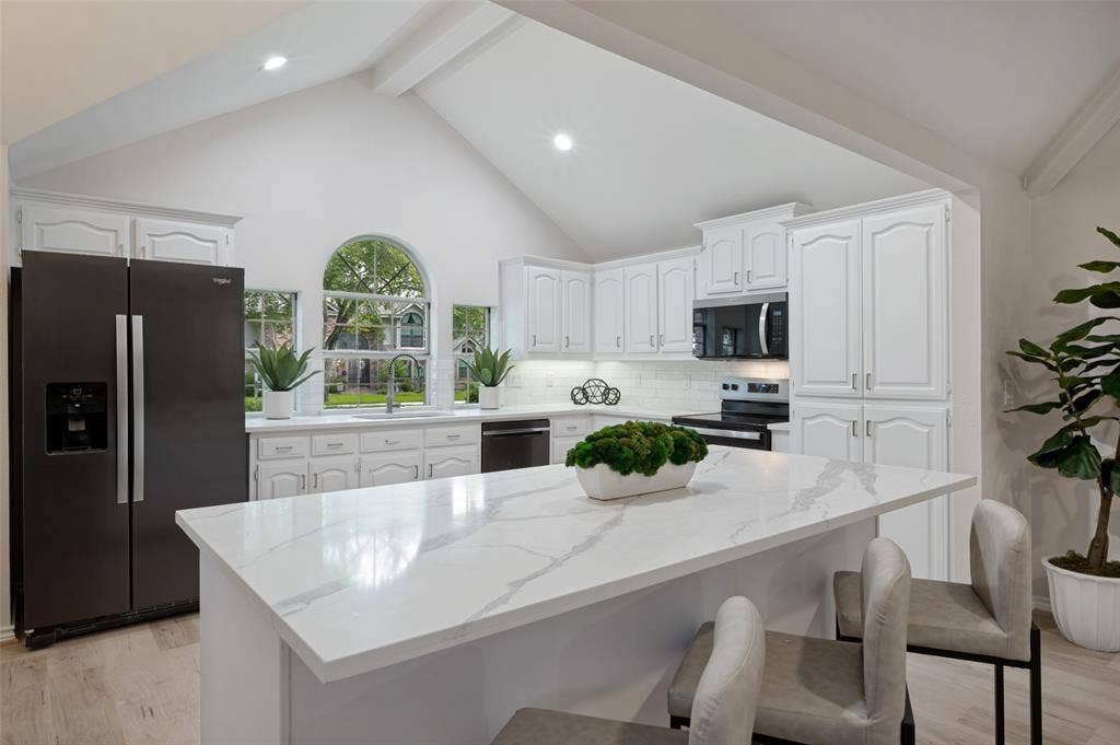 4420 Barwyn Lane, Plano, TX 75093 Kitchen featuring a central island with a stone-finish countertop, white cabinetry, vaulted ceilings, and an arched window above the sink