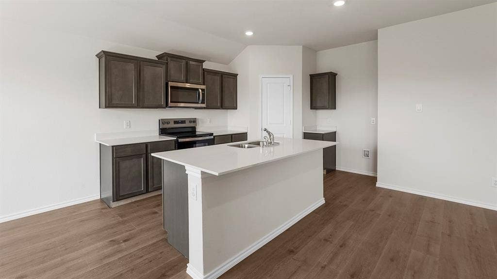 Kitchen featuring an island with a dual-basin sink, stainless steel appliances, dark wood-finish cabinetry, and light countertops