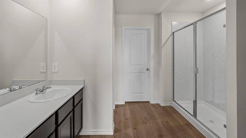 1969 Freeman Street, Tyler, TX 75702 Bathroom featuring a vanity with an integrated sink, a rectangular mirror, wood-finish flooring, a white paneled door, and a glass-enclosed shower