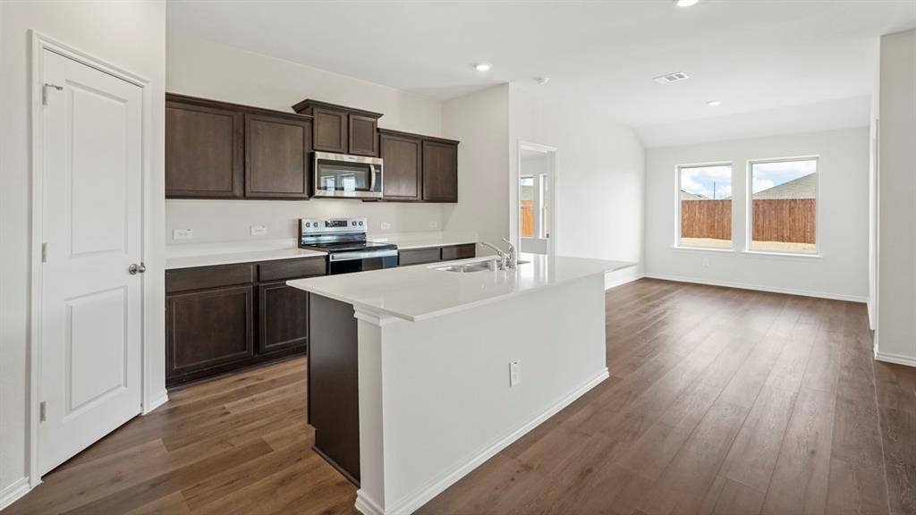 1969 Freeman Street, Tyler, TX 75702 Open-concept kitchen and living area featuring wood-finish flooring, dark wood cabinetry, stainless steel appliances, and white countertops