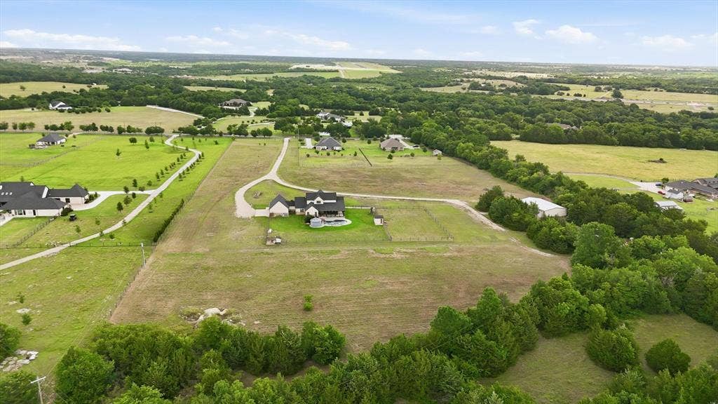 Expansive property featuring a large residence, swimming pool, gravel driveway, and surrounding green spaces