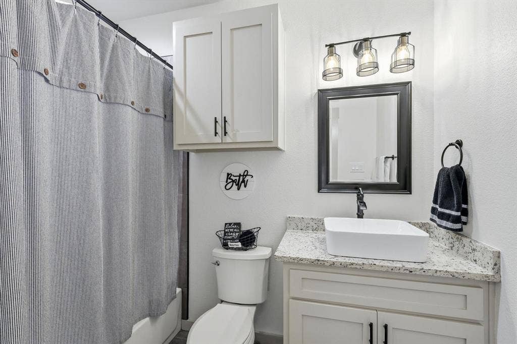 Bathroom featuring a vessel sink, stone-finish countertop, and white shaker-style cabinetry