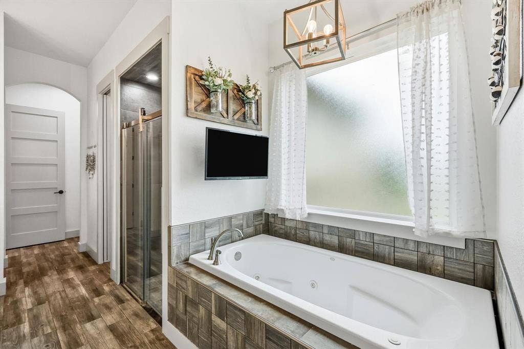 Jetted soaking tub with tile surround, paired with wood-look flooring, a framed glass shower enclosure, and a frosted privacy window