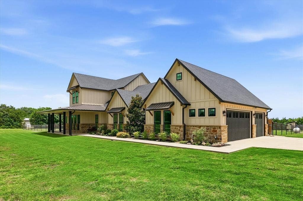 Contemporary farmhouse-style exterior featuring board and batten siding, a stone veneer foundation, a covered front porch with dark columns, dark-framed windows, and a two-car garage with dark paneled doors