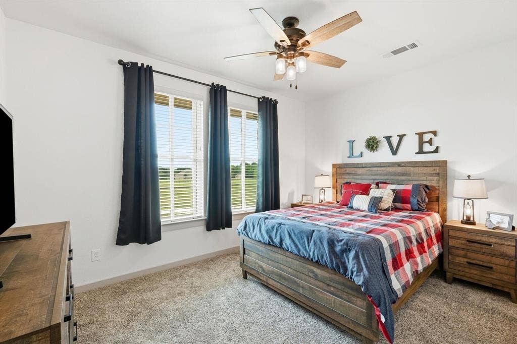 Carpeted bedroom featuring a ceiling fan with light fixture, dual windows, and light-colored walls