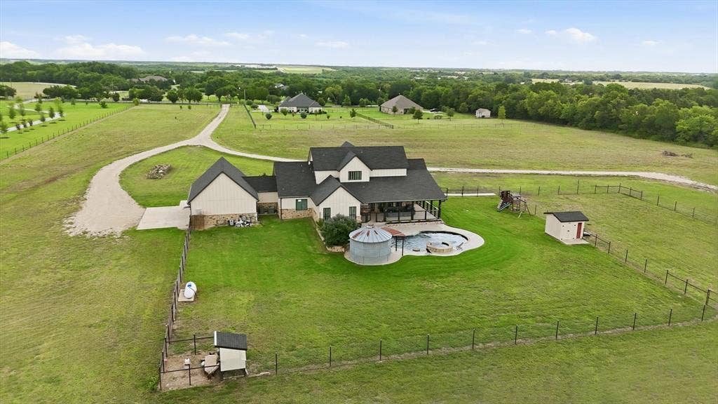 Expansive property featuring a multi-gable residence with an attached covered patio, a fenced backyard with an in-ground pool, and a gravel driveway