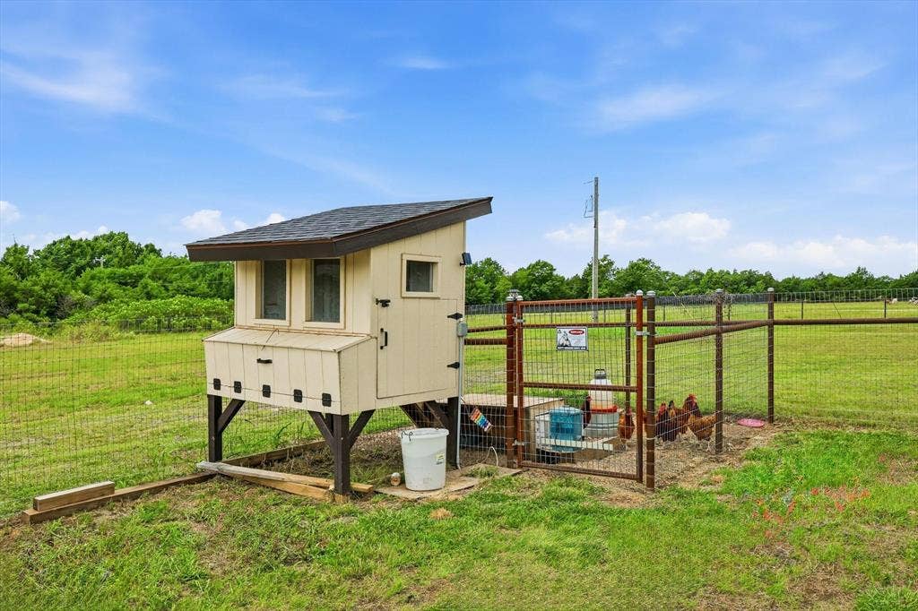 Elevated chicken coop featuring a shingled roof and multiple windows