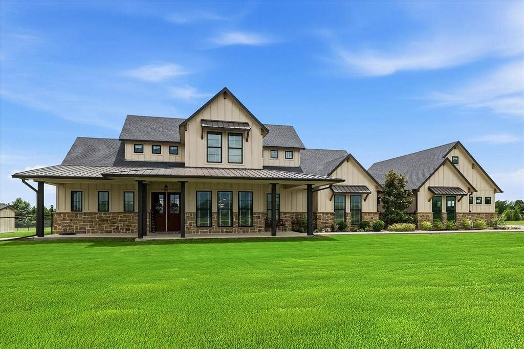 Expansive two-story residence featuring a covered front porch with dark pillars, light siding, and stone accents