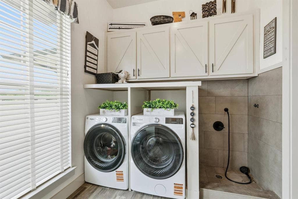 Dedicated laundry area featuring a built-in pet washing station, upper white cabinetry with barn door accents, and wood-finish flooring