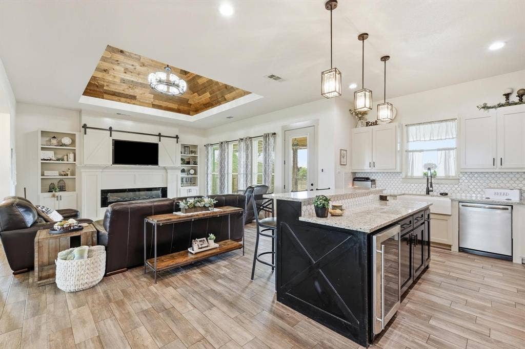 Open-concept living space featuring wood-finish flooring, a recessed ceiling with wood paneling, and a built-in electric fireplace with barn door accents
