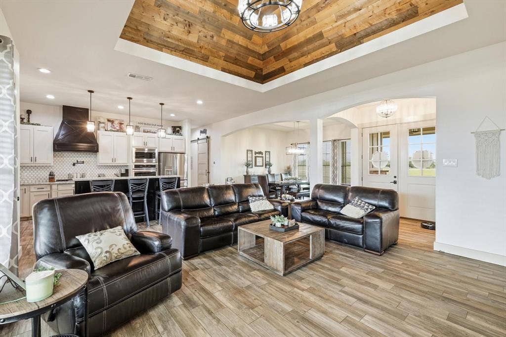 Living area featuring wood-finish flooring, a recessed ceiling with wood-paneled inlay, and a chandelier
