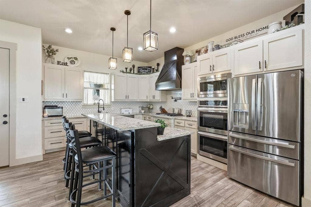 Gourmet kitchen featuring a large island with seating, stainless steel appliances, white cabinetry, granite countertops, and a decorative range hood