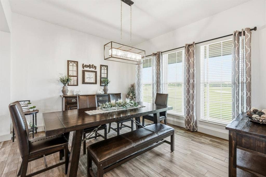Dining space featuring wood-finish flooring, a linear chandelier, and three large windows with blinds