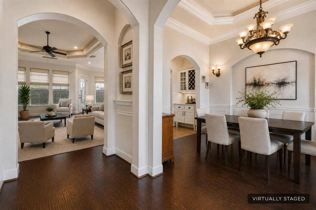 Dark wood-finish flooring throughout, tray ceiling with crown molding, and an elegant chandelier