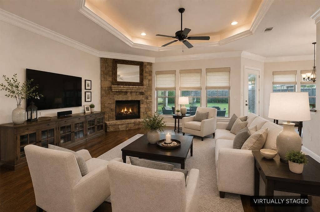 Stone-clad fireplace, tray ceiling with recessed lighting, wood-finish flooring, ceiling fan, and multiple windows